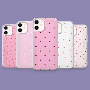 Puede incluir: Una colección de cinco fundas para teléfono en tonos rosa y blanco. Cada funda presenta un patrón de pequeños corazones en rojo o blanco. Las fundas están dispuestas en una fila, mostrando las diferentes combinaciones de colores y diseños.