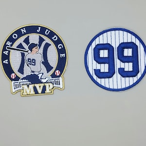 May include: Two embroidered patches. One is a navy blue and white patch with the text "AARON JUDGE" around a baseball player silhouette, the number "99", and the word "MVP". The other is a blue and white patch with the number "99".