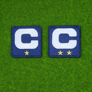 May include: Two navy blue embroidered patches with a white "C" and yellow stars. One patch has a single star, the other has two stars. The patches are square and set against a green background.