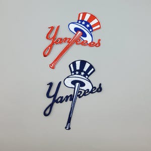 May include: Two embroidered patches featuring the word "Yankees" in script. One patch has a red script and a red, white, and blue Uncle Sam hat design. The other has a navy script and a navy and white hat design.