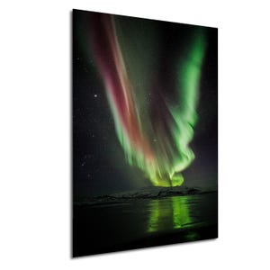 Puede incluir: Una impresión vibrante de la Aurora Boreal, mostrando una exhibición dinámica de luces verdes, rojas y púrpuras contra un cielo estrellado. La imagen captura el fenómeno natural sobre un paisaje nevado, con reflejos en el agua.