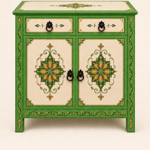 May include: A green wooden cabinet featuring two drawers and two doors with cream-colored panels. The piece is decorated with intricate gold and green geometric floral patterns, accented by black metal ring pulls on each drawer and door.