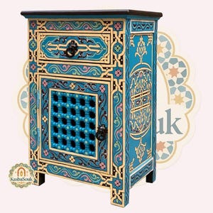 Può includere: Un comodino turchese dipinto a mano con intricati disegni floreali e geometrici in oro, nero e rosa. L'armadio presenta un cassetto, una porta con un motivo a griglia e ferramenta ornata. La parte superiore è marrone scuro.