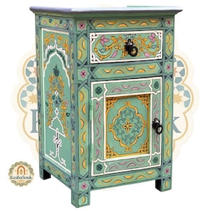 Könnte beinhalten: Ein handbemalter, grüner Nachttisch mit aufwendigen floralen und geometrischen Designs in Gelb, Weiß und Rosa. Der Schrank hat eine Schublade und eine Tür mit schwarzen Metallbeschlägen. Die Gesamthöhe beträgt ca. 61 cm.