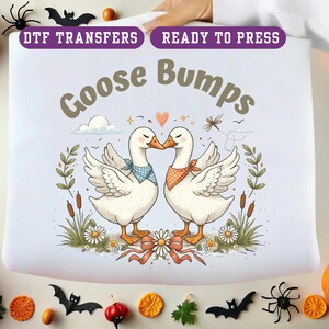 May include: A white DTF transfer with the words "Goose Bumps" above two kissing geese. The geese wear bandanas and stand in a field of flowers and reeds. Halloween decorations surround the transfer.