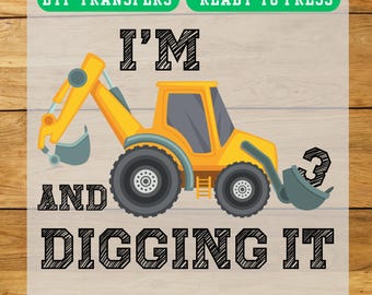 May include: A yellow and gray cartoon excavator with the text "I'M AND DIGGING IT" and the number "3". The image also includes the text "DTF TRANSFERS READY TO PRESS" and "EASY TO APPLY - FAST SHIPPING".