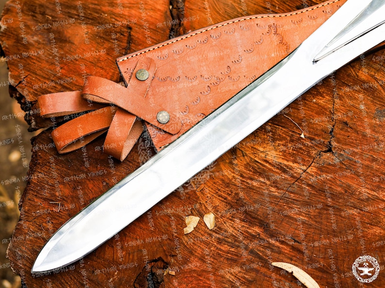 May include: A polished silver sword with a leather sheath and handle, resting on a textured wooden surface. The sheath is brown with decorative patterns and secured with a leather strap. The sword's blade is long and sharp.