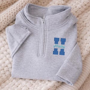 Könnte beinhalten: Ein Set aus drei Keramikbechern mit gesprenkelter, matter Oberfläche. Die Becher sind in Creme-, Hellgrau- und Dunkelgrautönen gehalten. Jeder Becher hat ein schlichtes, modernes Design und einen abgerundeten Henkel.