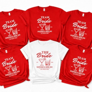 Puede incluir: Camisetas rojas y blancas con el texto "Team Bride" y "The Bride". Cada camiseta presenta un gráfico de cóctel y el texto "Sophia's Hen Do Las Vegas 2026".