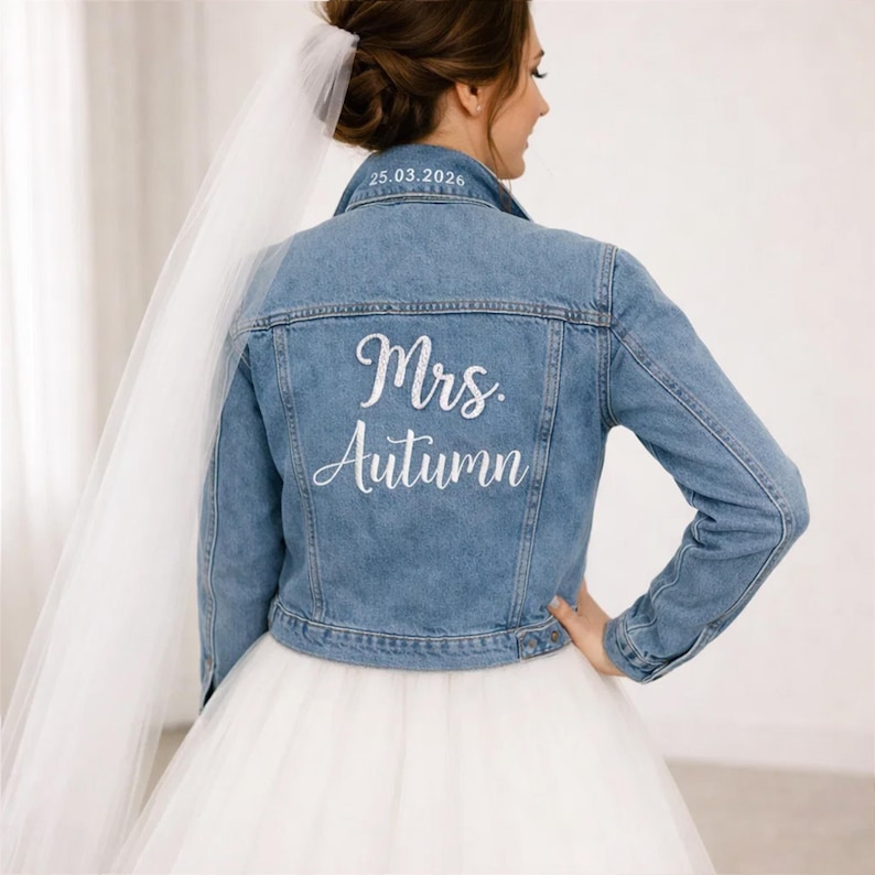 May include: Light blue denim jacket with the text "Mrs. Autumn" in white script on the back. The date "25.03.2026" is embroidered on the collar. The jacket is part of a bridal ensemble.