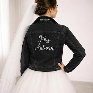 May include: Black denim jacket with the text "Mrs. Autumn" and the date "25.03.2026" printed on the back. The jacket has a classic design with button closures and a collar. The bride is wearing a white tulle skirt and veil.