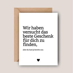 Könnte beinhalten: Eine weiße Grußkarte mit schwarzem Text, der lautet: "Wir haben versucht das beste Geschenk für dich zu finden, aber du hast ja bereits uns." Unten befindet sich ein kleines schwarzes Herz. Die Karte befindet sich in einem braunen Umschlag.