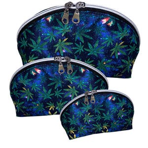 May include: Set of three cosmetic bags in varying sizes. Each bag features a dark blue background with a galaxy design and green cannabis leaves. The bags have silver zippers and white trim.