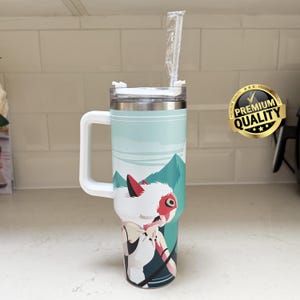 May include: A stainless steel travel mug with a white handle and lid. The mug features a design of a character with a white fur-like head, red accents, and a mountain landscape. A straw is inserted in the lid.
