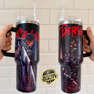 May include: Black insulated tumbler with a handle and a clear lid. The tumbler features a graphic of a character from the anime series "Berserk" on a black background. The tumbler also has a straw.