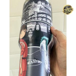 May include: A stainless steel tumbler featuring a black and white anime design. The artwork depicts scenes and characters from a popular animated film. The tumbler is cylindrical and has a glossy finish, with a gold "Premium Quality" sticker.