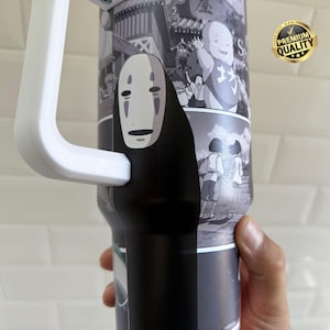 May include: A black and white tumbler featuring imagery from the animated film Spirited Away. The tumbler has a white handle and a black base. The design includes the character No-Face and other scenes from the movie. A gold "Premium Quality" sticker is visible.
