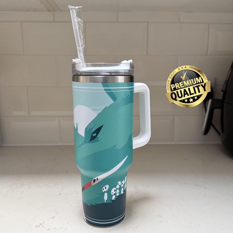 May include: A teal and silver insulated travel mug with a white handle and lid. The mug features a graphic of a wolf-like creature and a white straw. A gold "Premium Quality" sticker is on the right.