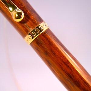 K&ouml;nnte beinhalten: Nahaufnahme eines Holzstiftes mit einem goldenen Band und einer goldenen Kappe. Der Stift hat eine dunkelbraune Holzmaserung.