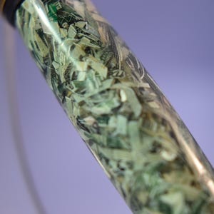 May include: A clear, cylindrical object filled with shredded U.S. dollar bills. The money is visible through the transparent material, creating a unique texture. The top of the object is black.