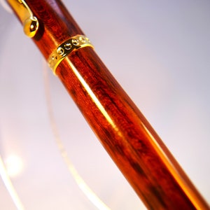 K&ouml;nnte beinhalten: Nahaufnahme eines Holzstiftes mit einem goldenen Band. Der Stift hat eine satte rotbraune Farbe und eine glatte, polierte Oberfl&auml;che.