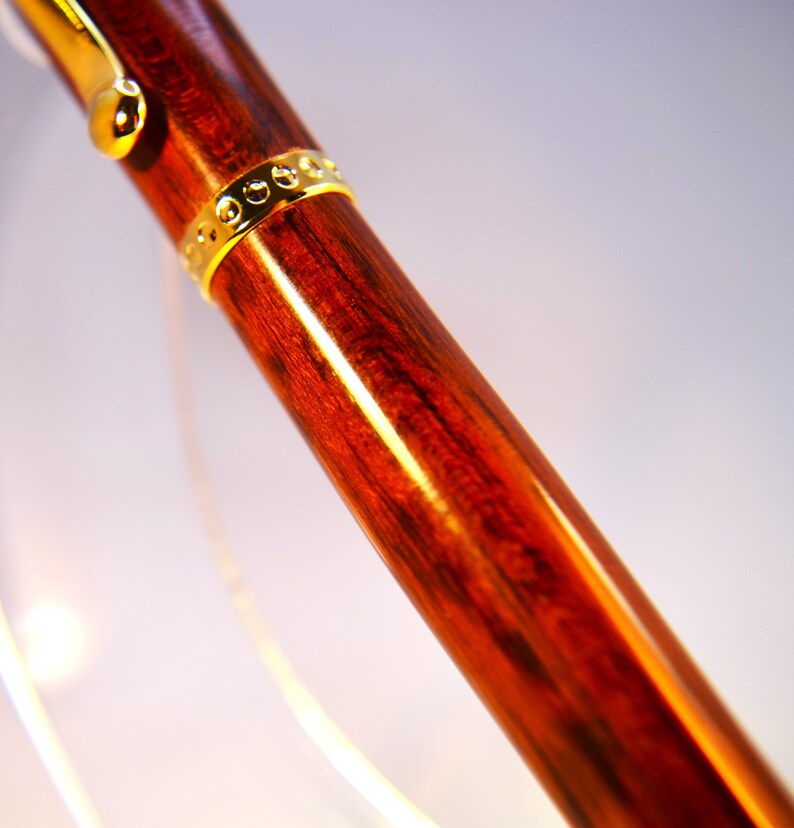 K&ouml;nnte beinhalten: Nahaufnahme eines Holzstiftes mit einem goldenen Band. Der Stift hat eine satte rotbraune Farbe und eine glatte, polierte Oberfl&auml;che.