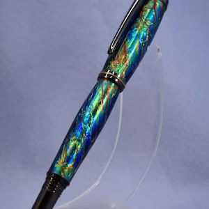 K&ouml;nnte beinhalten: Ein lebendiger F&uuml;llfederhalter mit einem Wirbelmuster aus Blau, Gr&uuml;n und Gold. Der Stift hat einen schwarzen Clip und Akzente sowie ein goldfarbenes Band. Der Stift wird auf einem transparenten St&auml;nder ausgestellt.