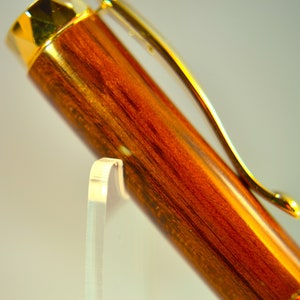 K&ouml;nnte beinhalten: Ein Holzstift mit goldfarbener Oberfl&auml;che und einem Clip. Der Stift hat ein r&ouml;tlich-braunes Holzmaserungsmuster.