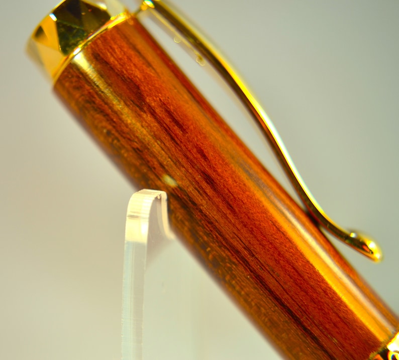 K&ouml;nnte beinhalten: Ein Holzstift mit goldfarbener Oberfl&auml;che und einem Clip. Der Stift hat ein r&ouml;tlich-braunes Holzmaserungsmuster.