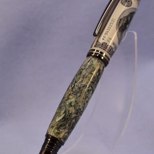 May include: A distinctive pen with a design incorporating elements of a US $100 bill. The pen has a black clip and tip, with a decorative band. The barrel is a mosaic of green and tan fragments, creating a textured appearance.