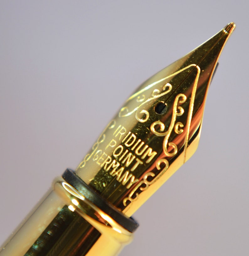 K&ouml;nnte beinhalten: Nahaufnahme einer goldfarbenen F&uuml;llfederhalter-Feder mit der Aufschrift "Iridium Point Germany".
