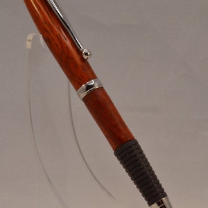 May include: A wooden pen with a silver clip and a black rubber grip. The pen is on a clear acrylic stand.