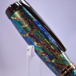 K&ouml;nnte beinhalten: Nahaufnahme eines F&uuml;llfederhalters mit schimmerndem, irisierendem Schaft. Der Stift weist eine Mischung aus blauen, gr&uuml;nen und goldenen Farben auf. Ein schwarzer Clip und goldene Akzente zieren den Stift, der leicht nach links geneigt ist.