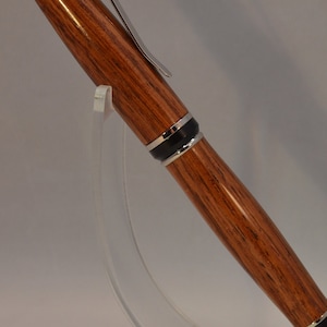 May include: A wooden pen with a silver clip and black accents. The pen is on a clear acrylic stand.