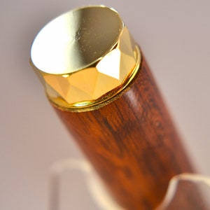 K&ouml;nnte beinhalten: Ein Holzstift mit einer goldfarbenen Kappe. Die Kappe hat ein facettierendes Design.