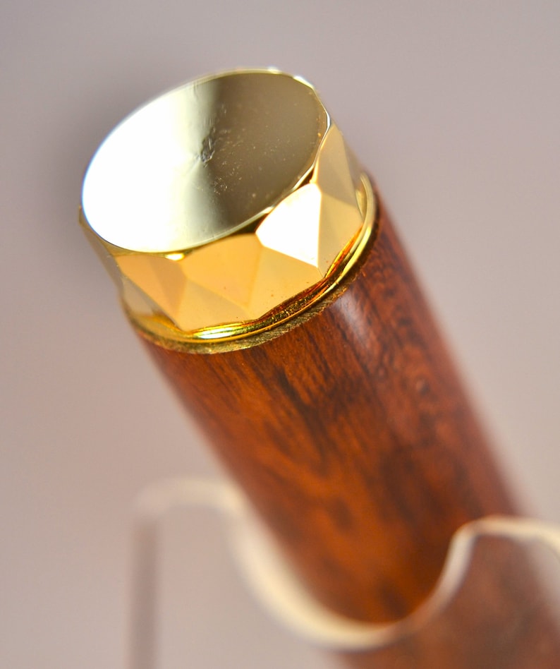 K&ouml;nnte beinhalten: Ein Holzstift mit einer goldfarbenen Kappe. Die Kappe hat ein facettierendes Design.