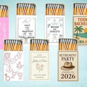 May include: A selection of matchboxes with different designs. One is pink with "Happy Birthday" text. Others have wedding, anniversary, and retirement themes, with text and illustrations. Each box contains matches with grey tips.