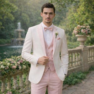 May include: A formal suit featuring a cream-colored jacket with a pink lapel, a matching pink vest, and pink trousers. The ensemble is completed with a pink bow tie, white dress shirt, and white shoes. A boutonniere adds a floral accent.