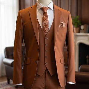 May include: A three-piece suit in a warm brown hue, displayed on a mannequin. The suit includes a jacket, vest, and trousers, paired with a white dress shirt and a patterned tie. A pocket square complements the ensemble. The suit is tailored for a formal occasion.