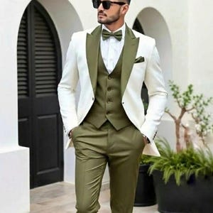 May include: A three-piece suit featuring a white jacket with olive green lapels, a matching vest, and olive green trousers. The suit includes a white dress shirt and an olive green bow tie. The person is wearing black sunglasses.