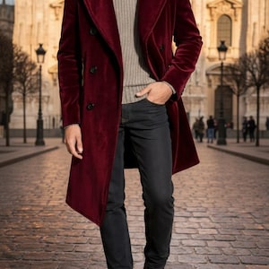 May include: A burgundy velvet overcoat with a double-breasted design. The coat is worn over a gray turtleneck sweater and dark jeans. The person is wearing brown leather boots. The background features a European city street.