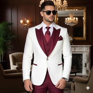 May include: A formal white suit with a burgundy vest, tie, and pocket square. The suit features a two-button closure and is paired with matching burgundy pants. The man is wearing sunglasses and a watch.