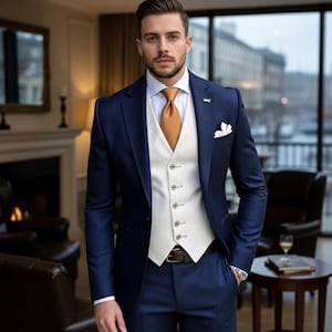 May include: A navy blue suit with a white waistcoat and a gold tie. The suit is well-tailored, with a pocket square and a brown belt. The man is in a room with a fireplace and large windows, with a view of the city.