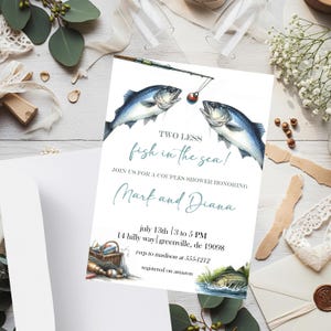 Può includere: Un biglietto d'invito bianco con il testo "TWO LESS fish in the sea!" e "Mark and Diana" in corsivo turchese. Il biglietto presenta illustrazioni ad acquerello di pesci, una canna da pesca e un cesto da pesca, perfetto per un baby shower.