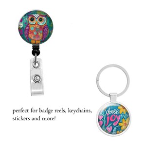Pode incluir: Um porta-crach&aacute; com um design de coruja colorido e um porta-chaves com as palavras "choose joy" rodeadas de flores. O porta-crach&aacute; de coruja &eacute; azul-petr&oacute;leo, roxo e laranja. O porta-chaves tem um anel prateado.