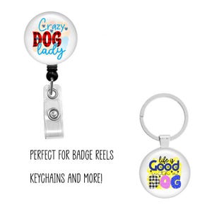 Puede incluir: Un portatarjetas con el texto "Crazy Dog Lady" y un llavero con el texto "life is Good with a Dog". El portatarjetas tiene un clip de pl&aacute;stico transparente y un cable retr&aacute;ctil negro. El llavero tiene un anillo plateado.