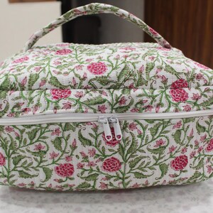May include: A floral print cosmetic bag with a white zipper and handle. The bag features a pattern of pink flowers and green leaves on a white background. The bag is rectangular with rounded edges.