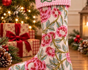May include: A quilted Christmas stocking featuring a pink and white striped cuff with the name Lisa embroidered in green script. The body of the stocking has a cream background with a repeating pattern of pink flowers and green leaves.