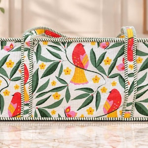 May include: A rectangular fabric storage bag featuring a white background with a repeating pattern of red birds with yellow tails, green leaves, small yellow flowers, and pink butterflies. The bag has two fabric handles and green striped trim.