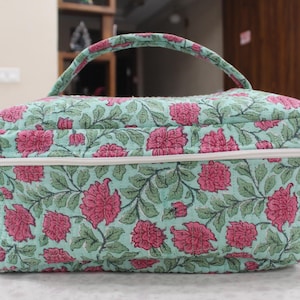 May include: A rectangular cosmetic bag with a handle, featuring a floral pattern of pink flowers and green leaves on a light blue background. The bag has a white zipper and trim.